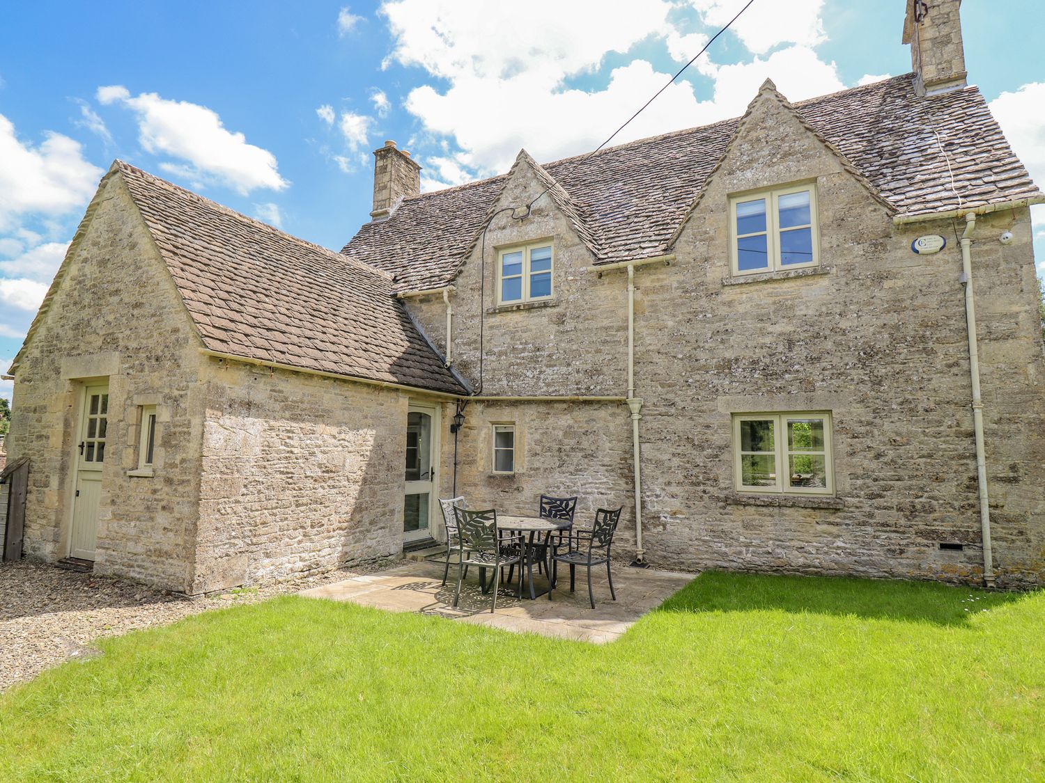 A stone house with a small patio and metal table and chairs on a green lawn at No 1 Eastington in Eastington near Northleach