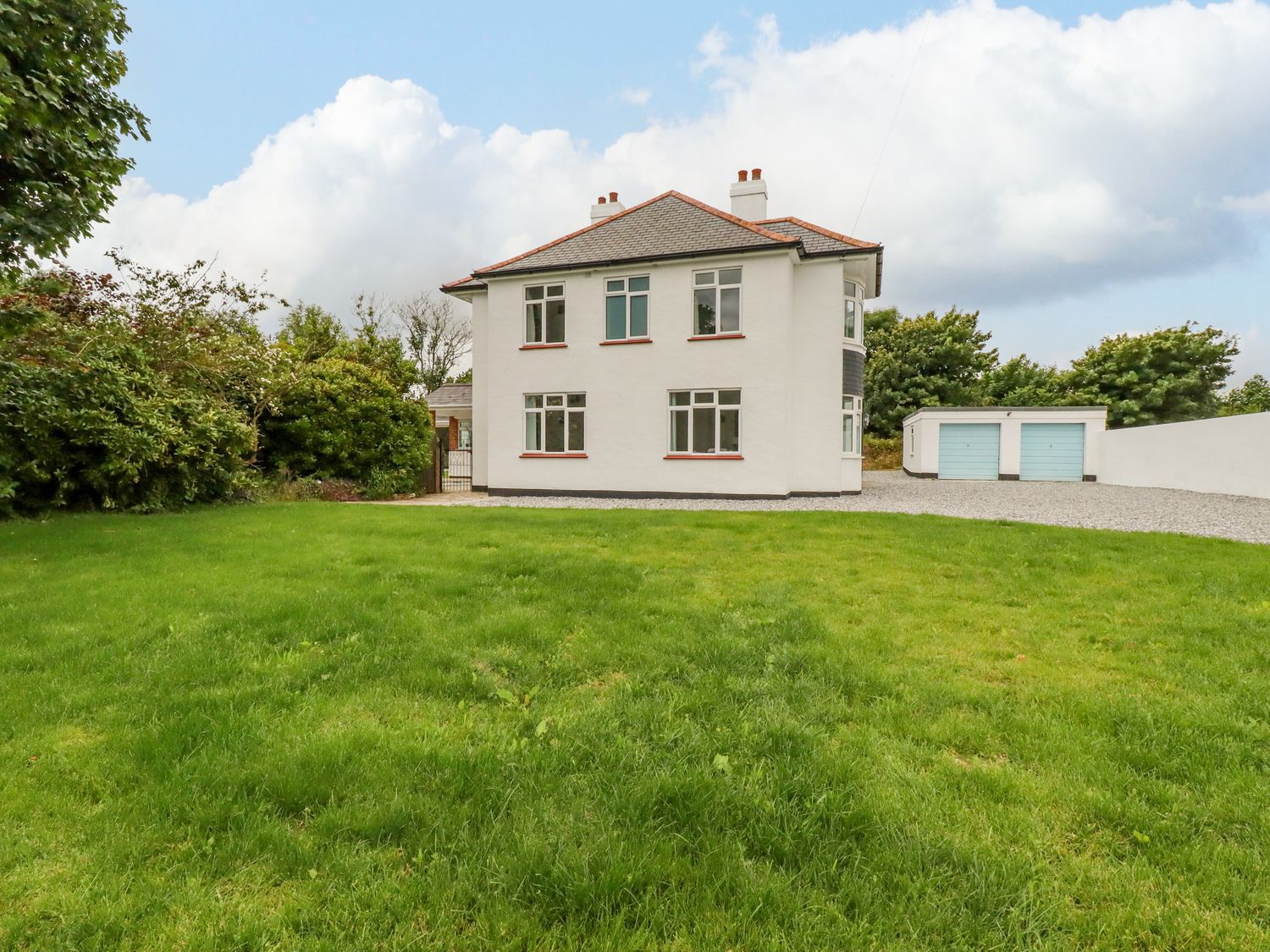 A two story house with white walls and a gray roof a green lawn in front and two blue garage doors on the right at Pen-Y-Thon House in Summercourt