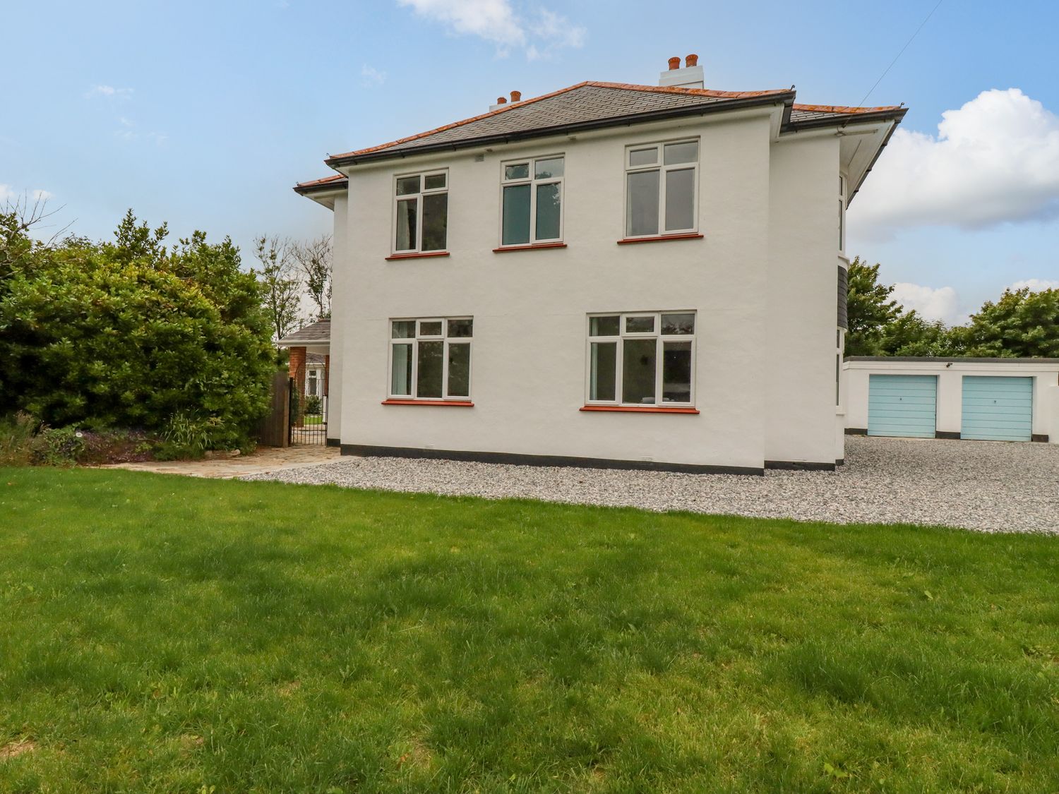 Exterior of a two story house with white walls and windows near a lawn and garages at Pen-Y-Thon House in Summercourt