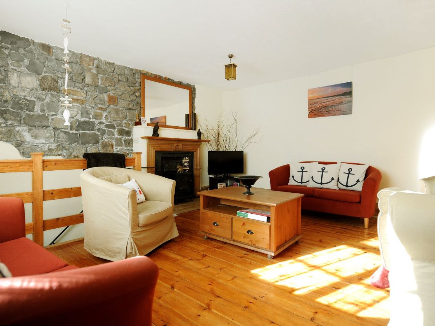 A living room with wooden floor a stone wall a fireplace armchairs a wooden coffee table and a red sofa with anchor cushions at Waltham House in Lyme Regis