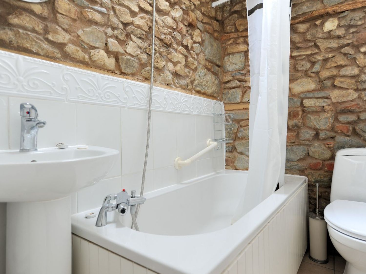 A bathroom with a bathtub a shower curtain a sink and a toilet with stone walls at Waltham House Lyme Regis