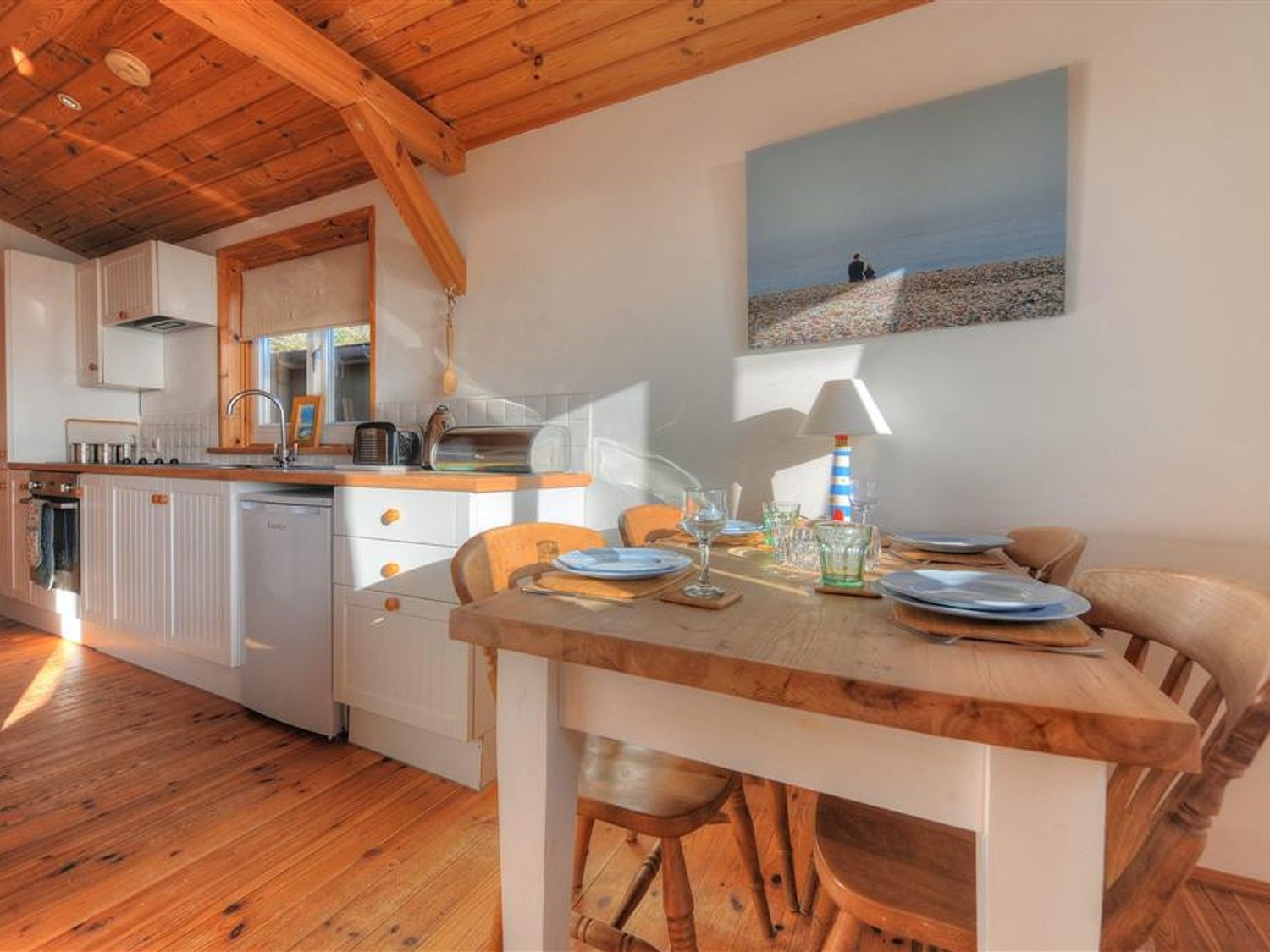 A kitchen with wooden ceiling and floor a dining table with plates and glasses and kitchen appliances at St Anton in Lyme Regis