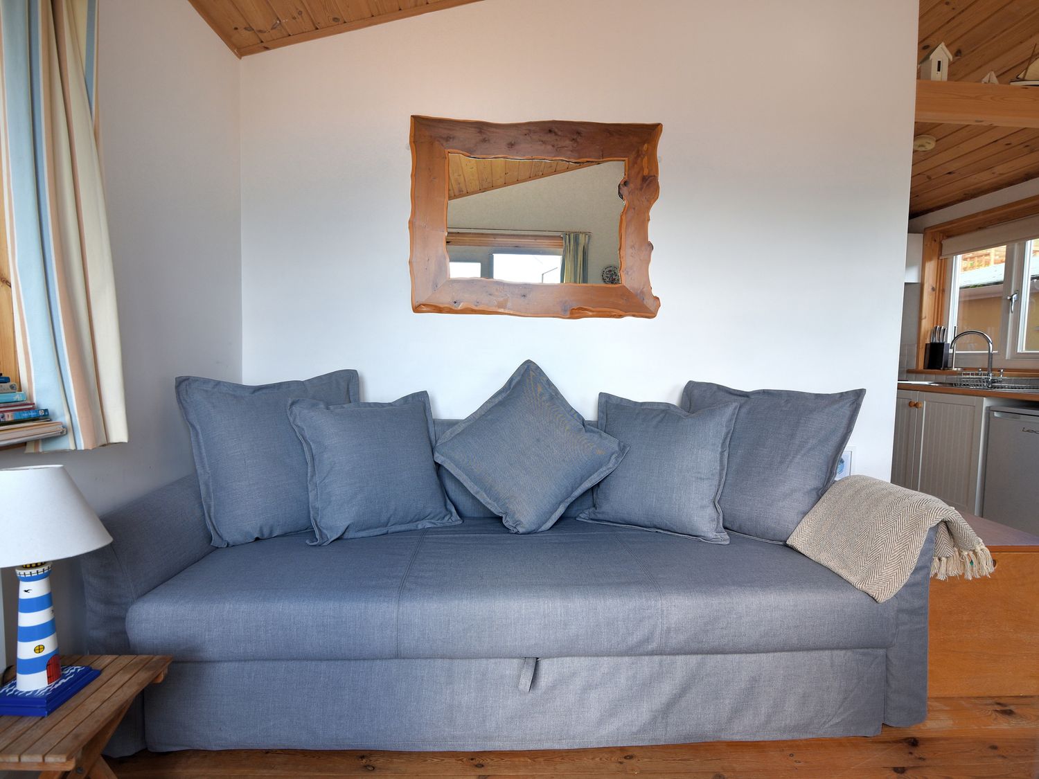 A blue sofa with five cushions and a blanket a wooden framed mirror above the sofa and a wooden side table with a lamp at St Anton Lyme Regis