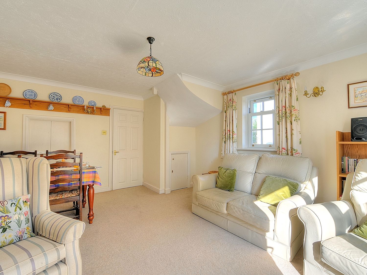A living room with a sofa, armchairs, a dining table with chairs, a bookshelf, and a window with curtains at Blacksmiths Cottage in Lyme Regis