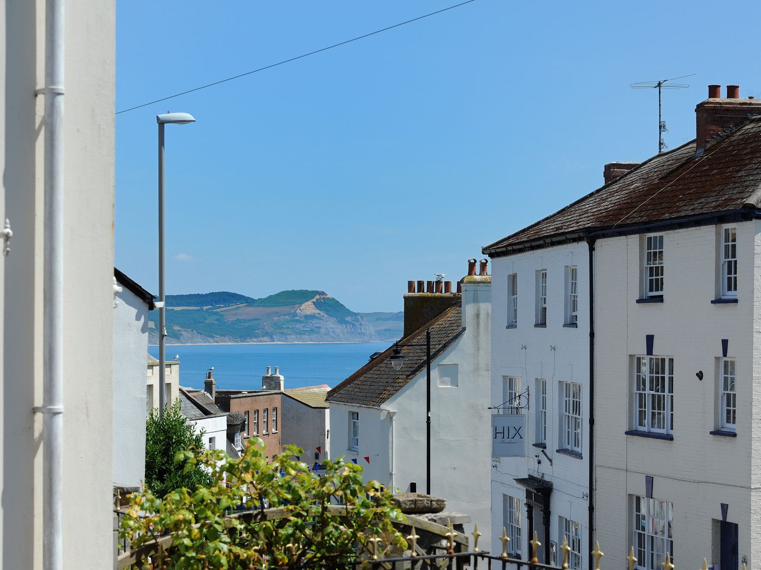 A coastal street with white buildings and a view of the sea and hills in the background at Blacksmiths Cottage in Lyme Regis
