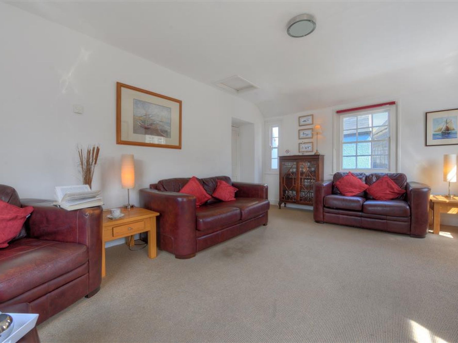 A living room with brown leather sofas red cushions wooden side tables lamps framed pictures and a wooden cabinet at Riverview in Lyme Regis
