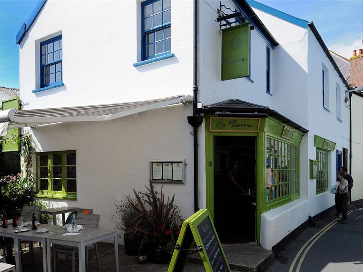 The exterior of a white building with blue window frames and green shopfronts with tables and chairs outside at Riverview in Lyme Regis