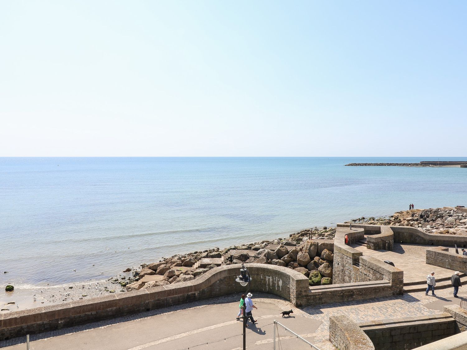 A seaside view with a promenade and people walking at Watersmeet Lyme Regis