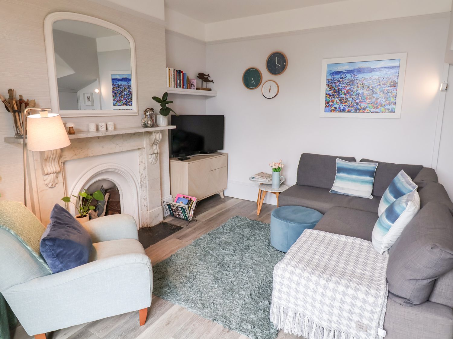 A living room with a gray sofa with pillows a light armchair a rug and a TV near a fireplace at Sea Glass in Lyme Regis
