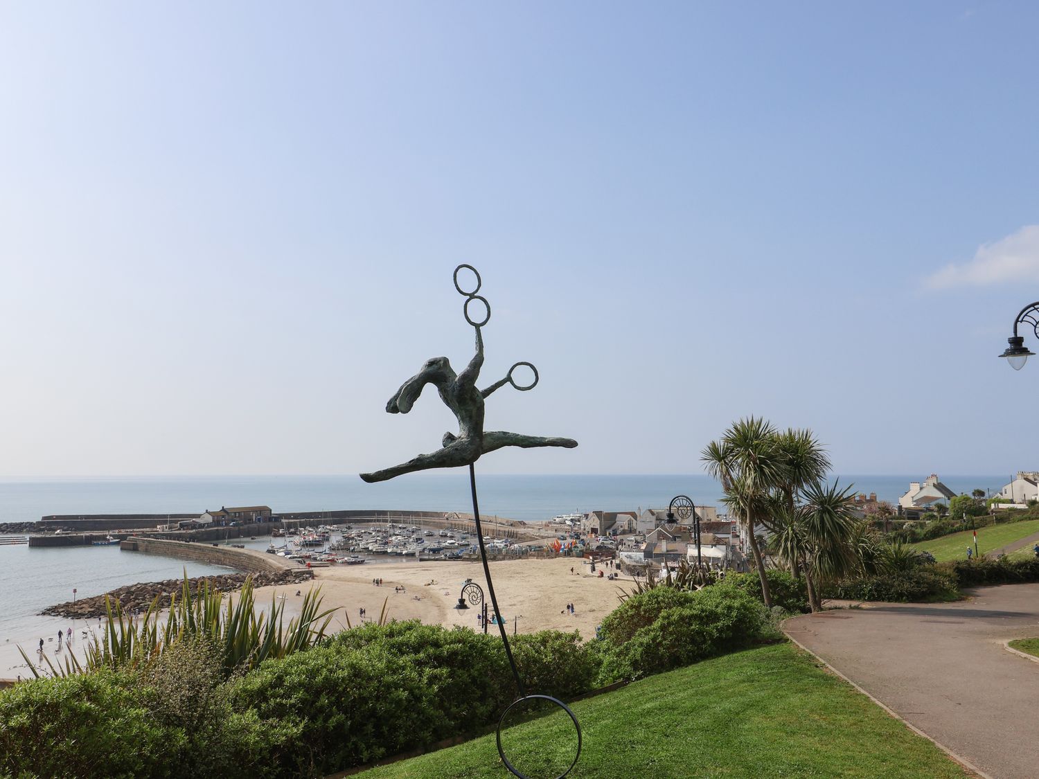 A coastal view with a sculpture of a person jumping with rings a beach marina and houses in the background at Grannys Teeth in Lyme Regis