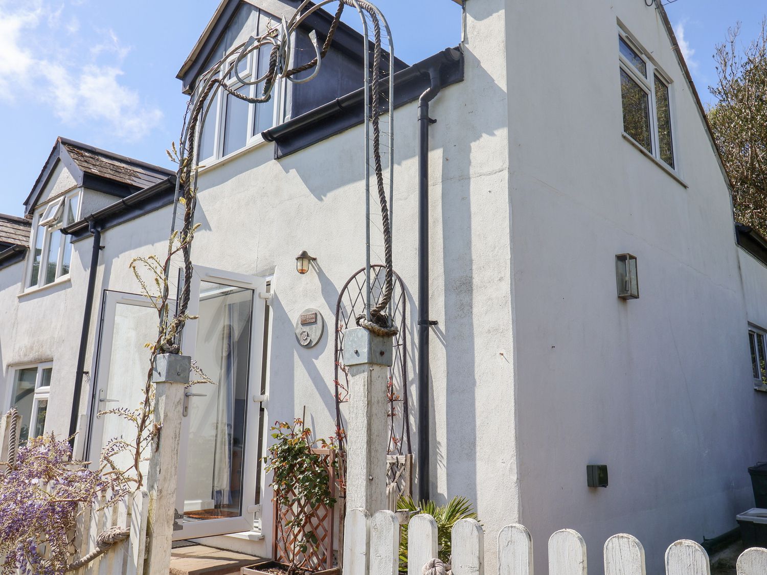 Exterior view of a white house with open glass door and metal arch at High Bullen Cottage in Morcombelake