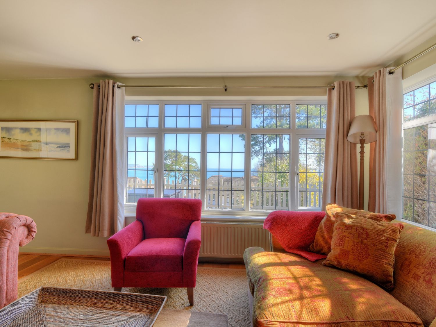 A living room with a red armchair an orange sofa and large windows with a view at Westhaven in Lyme Regis