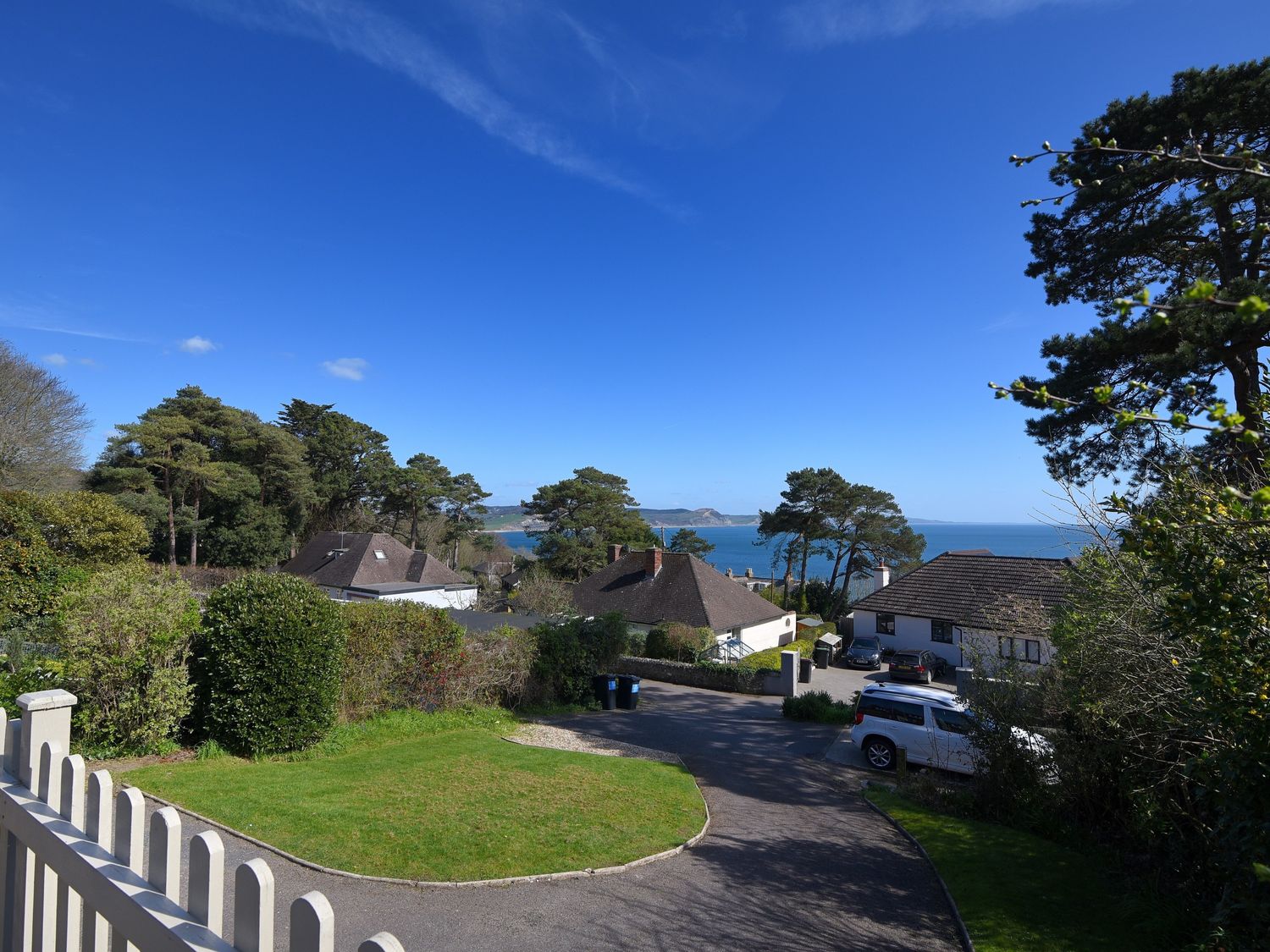 A coastal residential area with houses trees and parked cars overlooking the sea at Westhaven in Lyme Regis