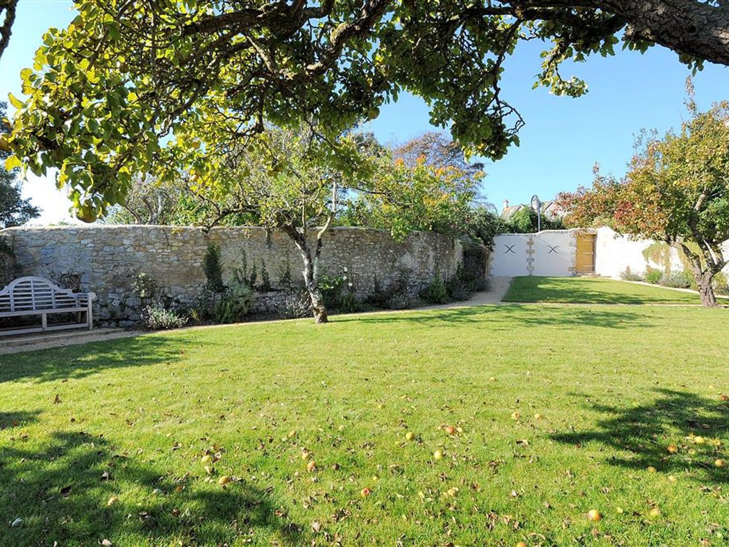 A garden with trees a wooden bench a stone wall and a gated entrance at Seashell in Lyme Regis