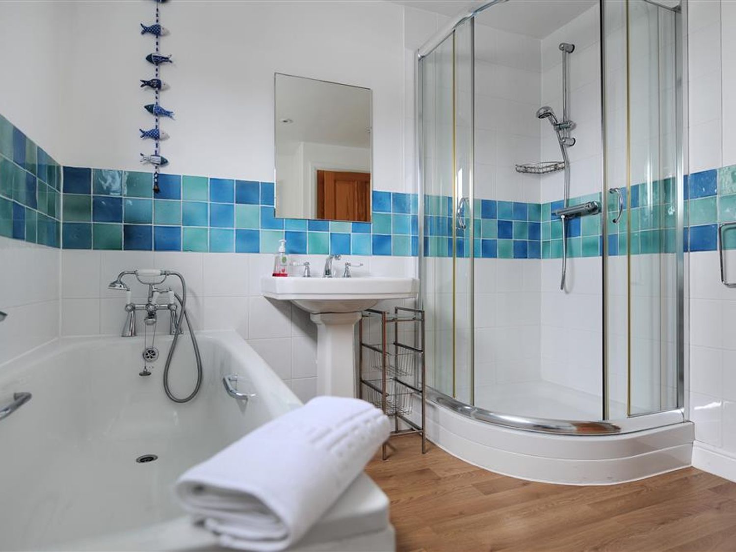 A bathroom with a bathtub sink and shower enclosure with blue and green tiled walls at Rooftops Lyme Regis