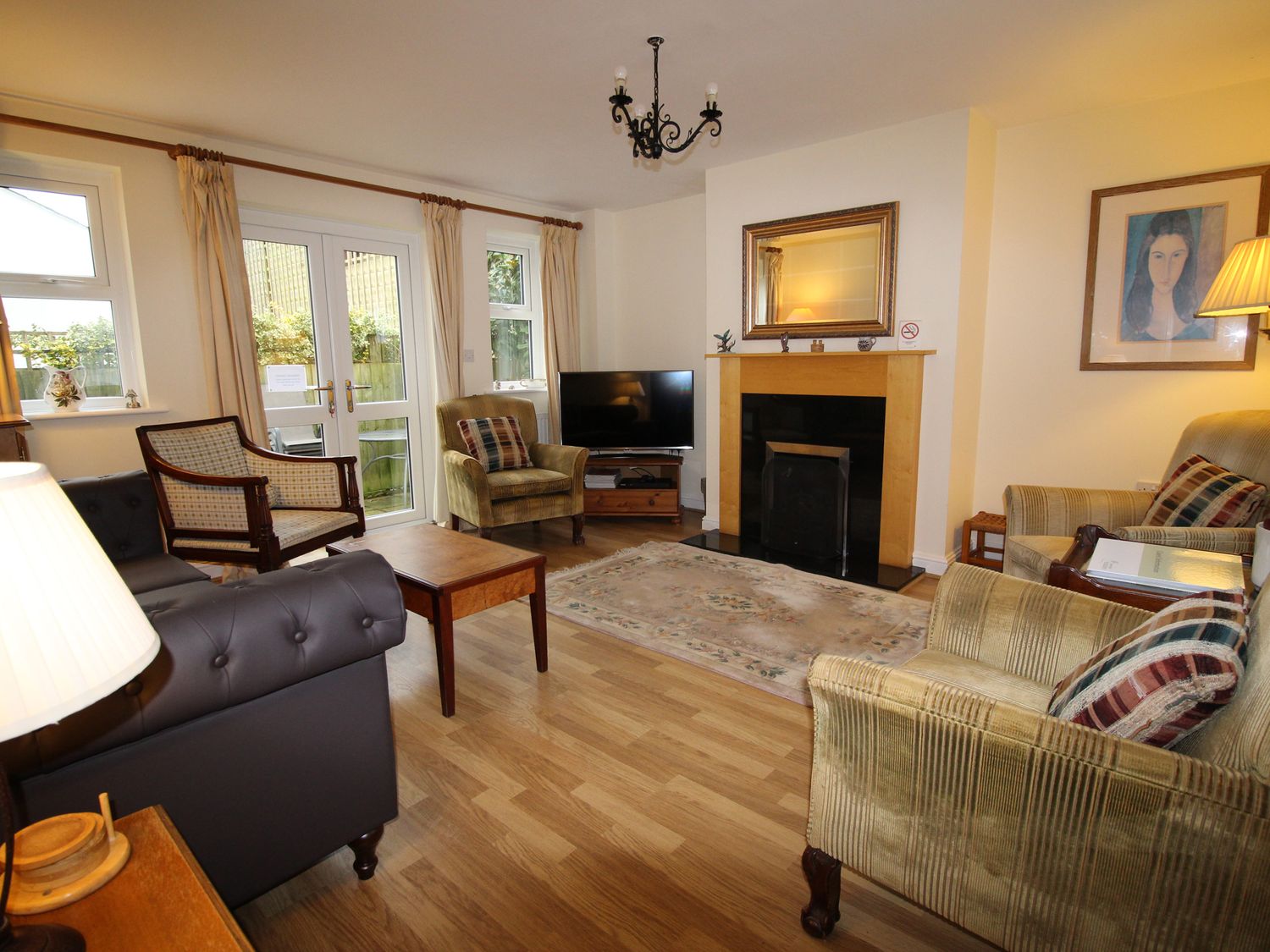 A living room with armchairs a sofa a coffee table a fireplace a television and double doors at Vine Cottage in Charmouth