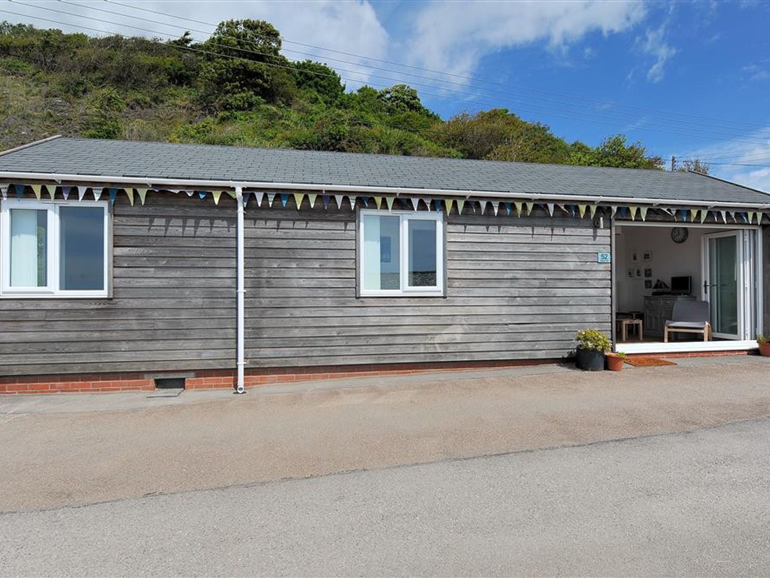 A wooden single-story house with two windows and an open door with bunting above at The Beach Hut in Lyme Regis