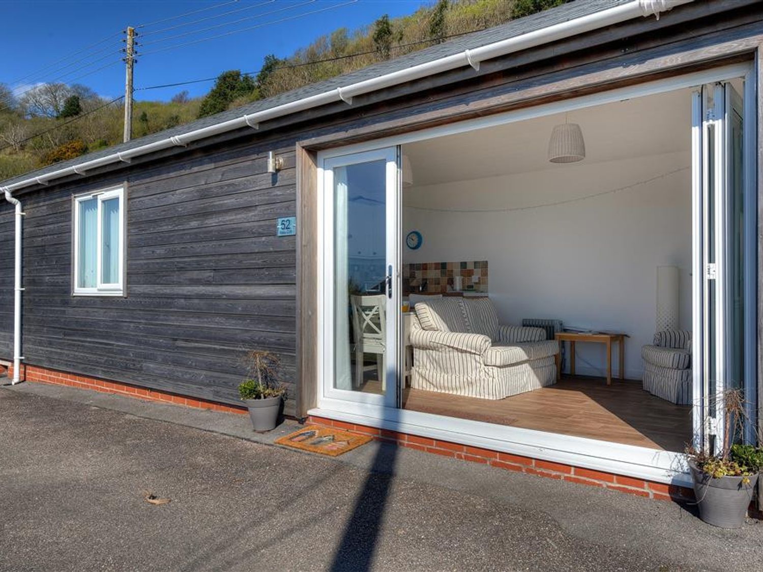 A cabin exterior with an open sliding door showing a living room with striped armchairs at The Beach Hut in Lyme Regis