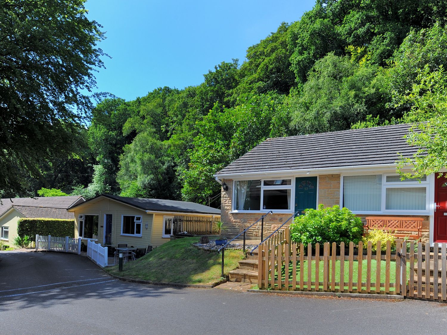 A residential street with one house and a small building surrounded by trees at 36 Fernhill Heights in Charmouth