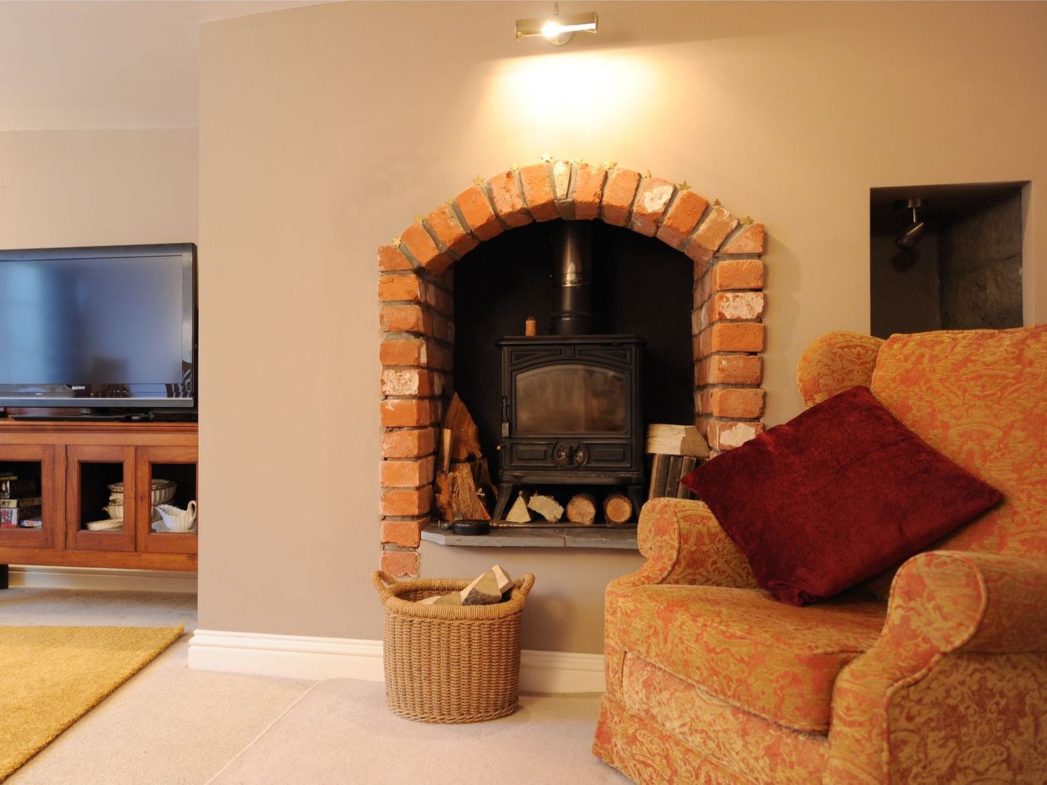 A living room with a wood stove in a brick fireplace and an armchair with a red cushion at Tudor Cottage in Lyme Regis