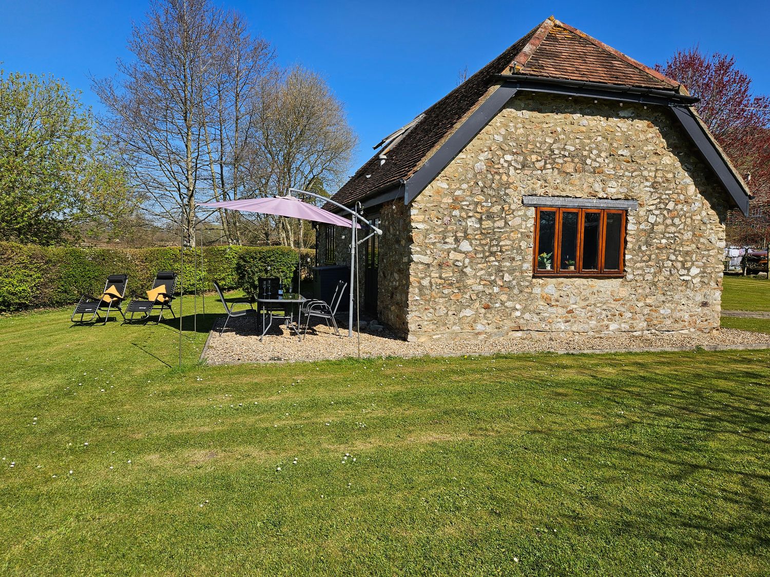 A stone cottage with outdoor chairs and a table with an umbrella on a lawn at The Cider House in Dalwood