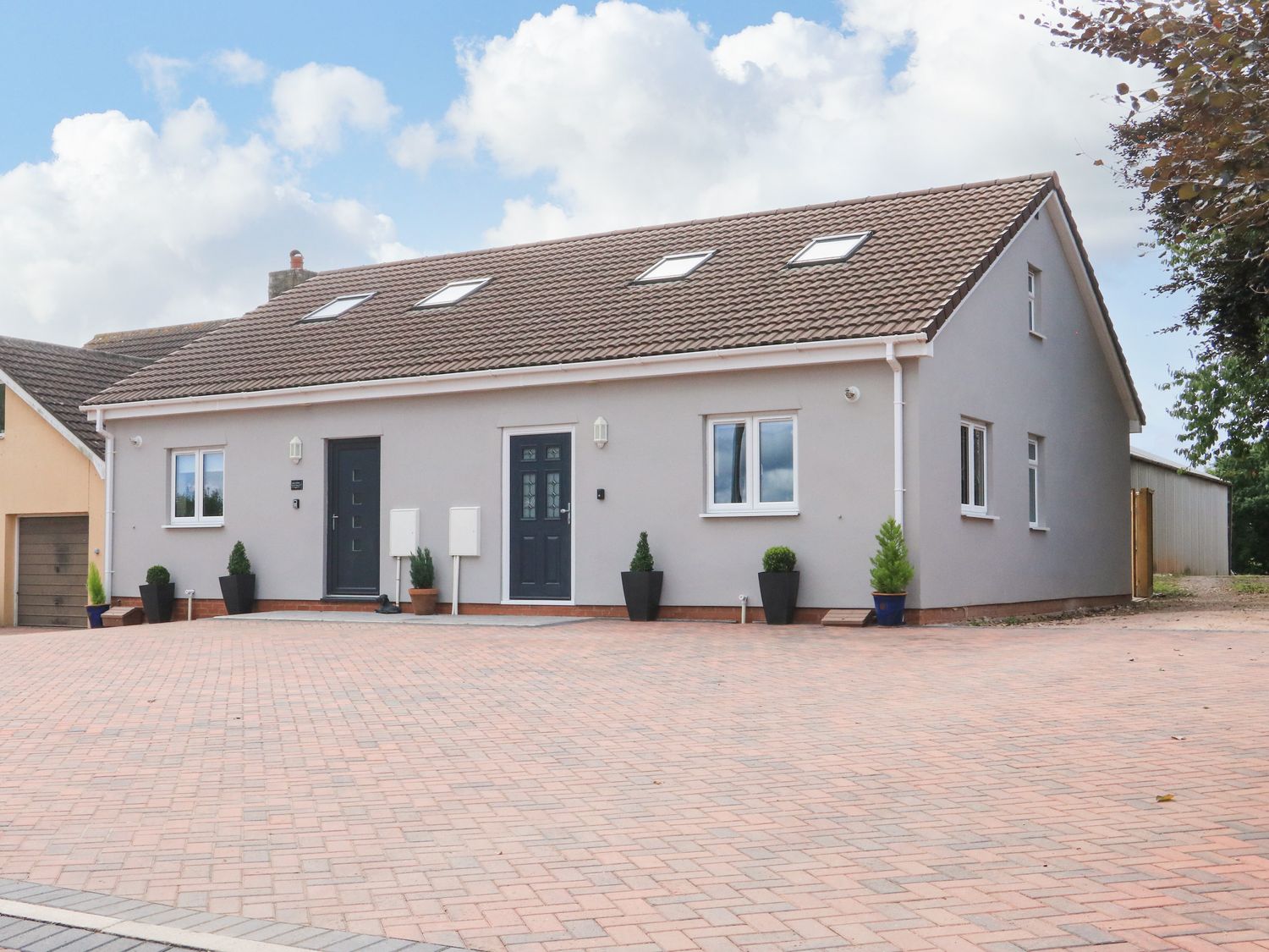 A brick paved driveway in front of a two door gray house with skylights and potted plants at Sawtons Cottage 2 in Dawlish