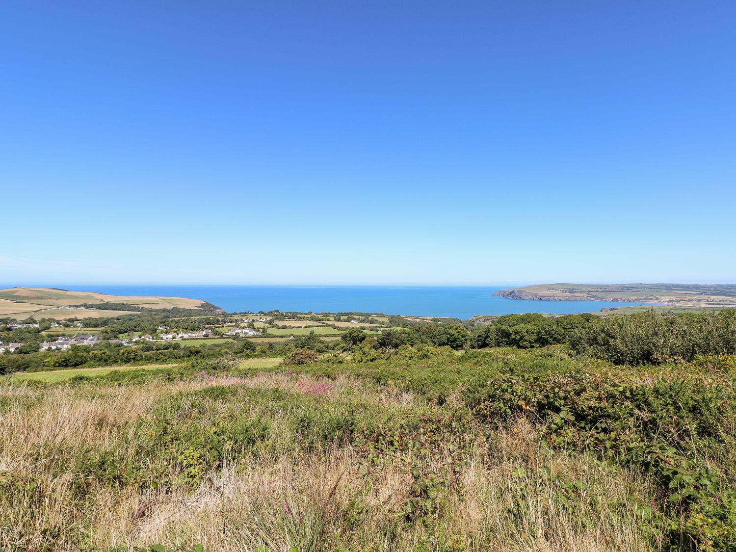 A coastal landscape with grassy fields and a small village near the sea at Arfron in Dinas Cross