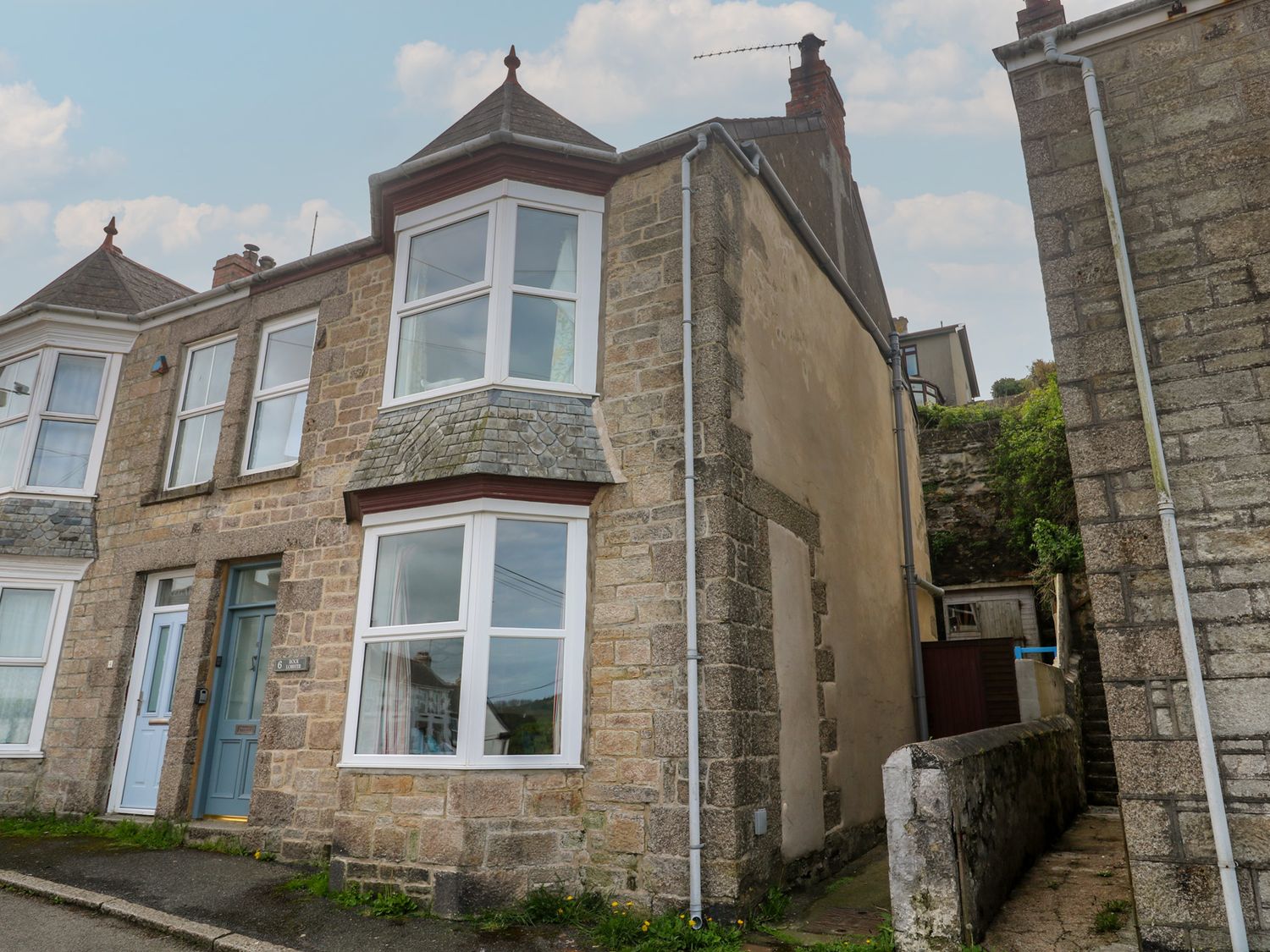 Stone terraced houses with bay windows and railings along a narrow street in Porthleven