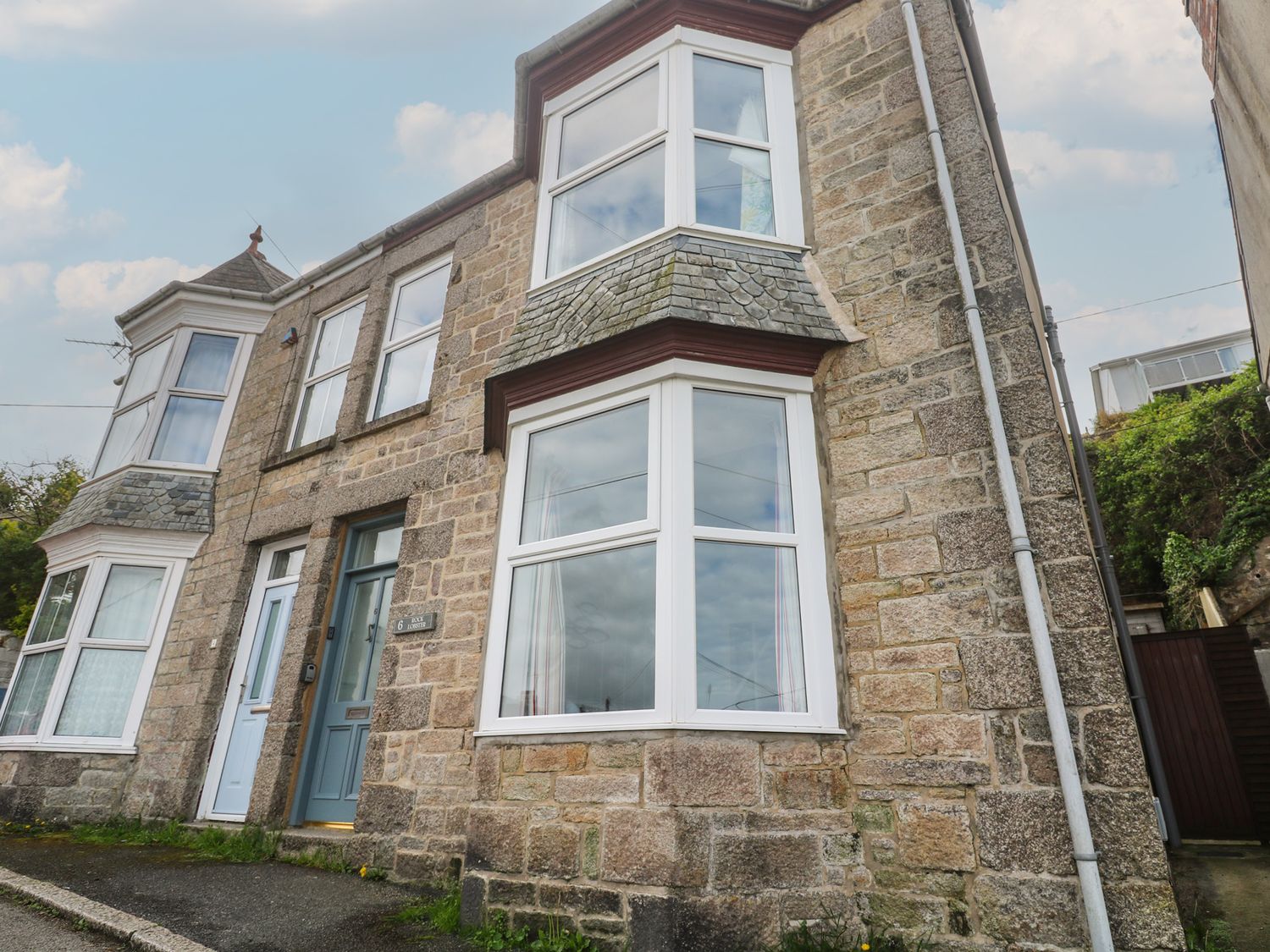 A stone exterior of a house with bay windows and a blue door at Rock Lobster in Porthleven