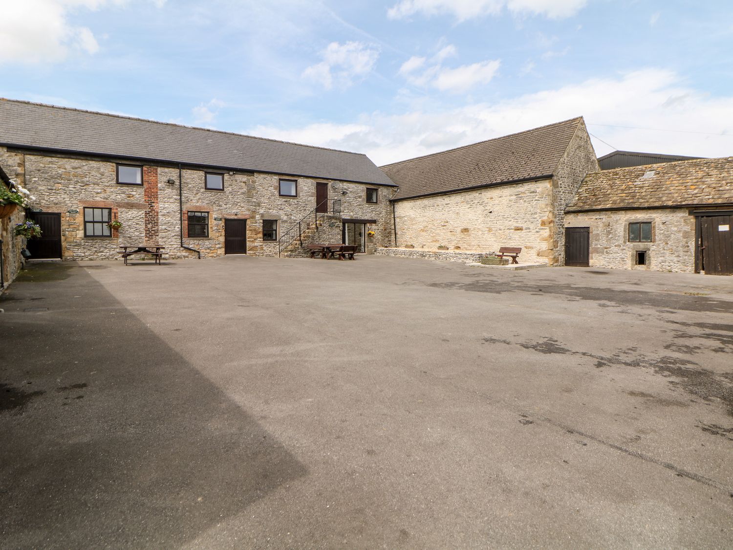 A large paved courtyard surrounded by stone buildings with wooden doors and benches at Brendan in Bakewell