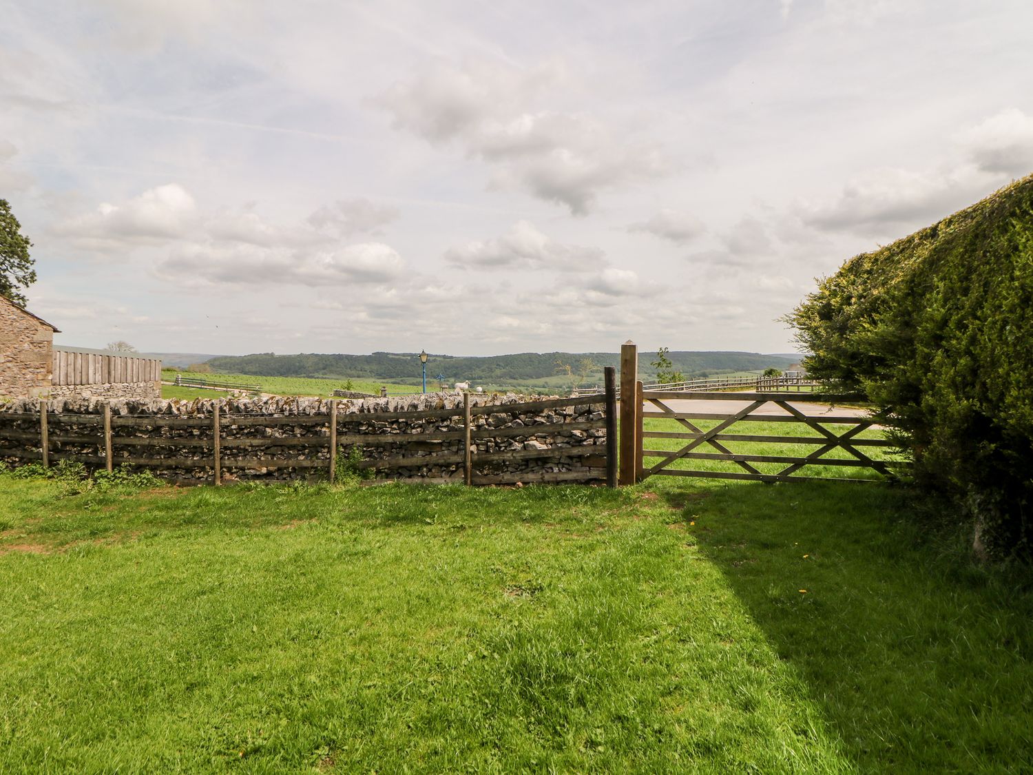 A grassy yard with a wooden gate and stone fence with hills in the background at Brendan in Bakewell