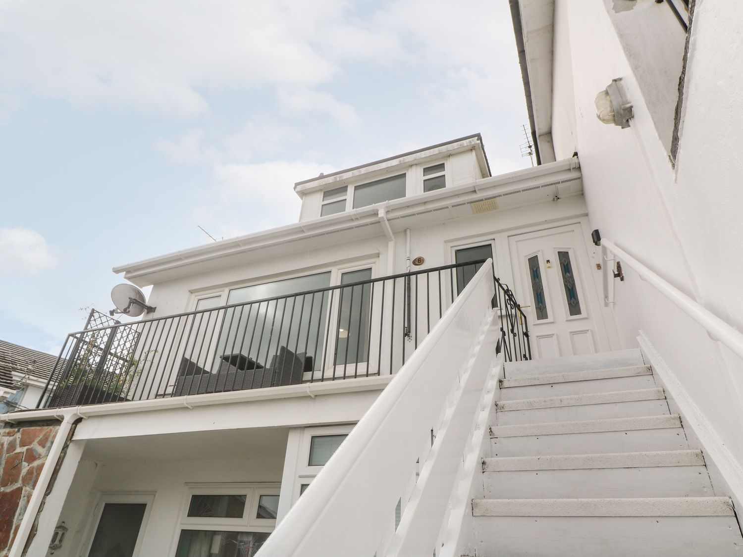 Exterior view of a white building with stairs leading to a door and a balcony with black railing at Flat 6 in Falmouth