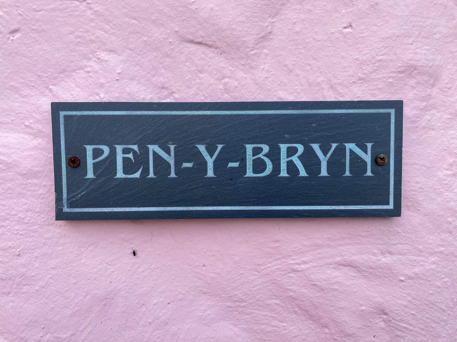 A black and white house name sign reading PEN-Y-BRYN on a pink textured wall at Pen- y- Bryn @ Canllefaes in Penparc near Cardigan
