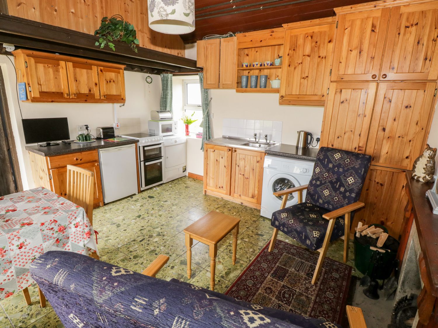 A kitchen with wooden cabinets, a small dining table, chairs, a washing machine, and a sofa at The White House in Roundstone, County Galway