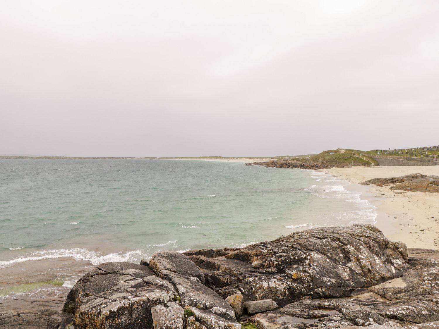 A rocky shoreline with waves on a sandy beach under a cloudy sky at The White House in Roundstone County Galway