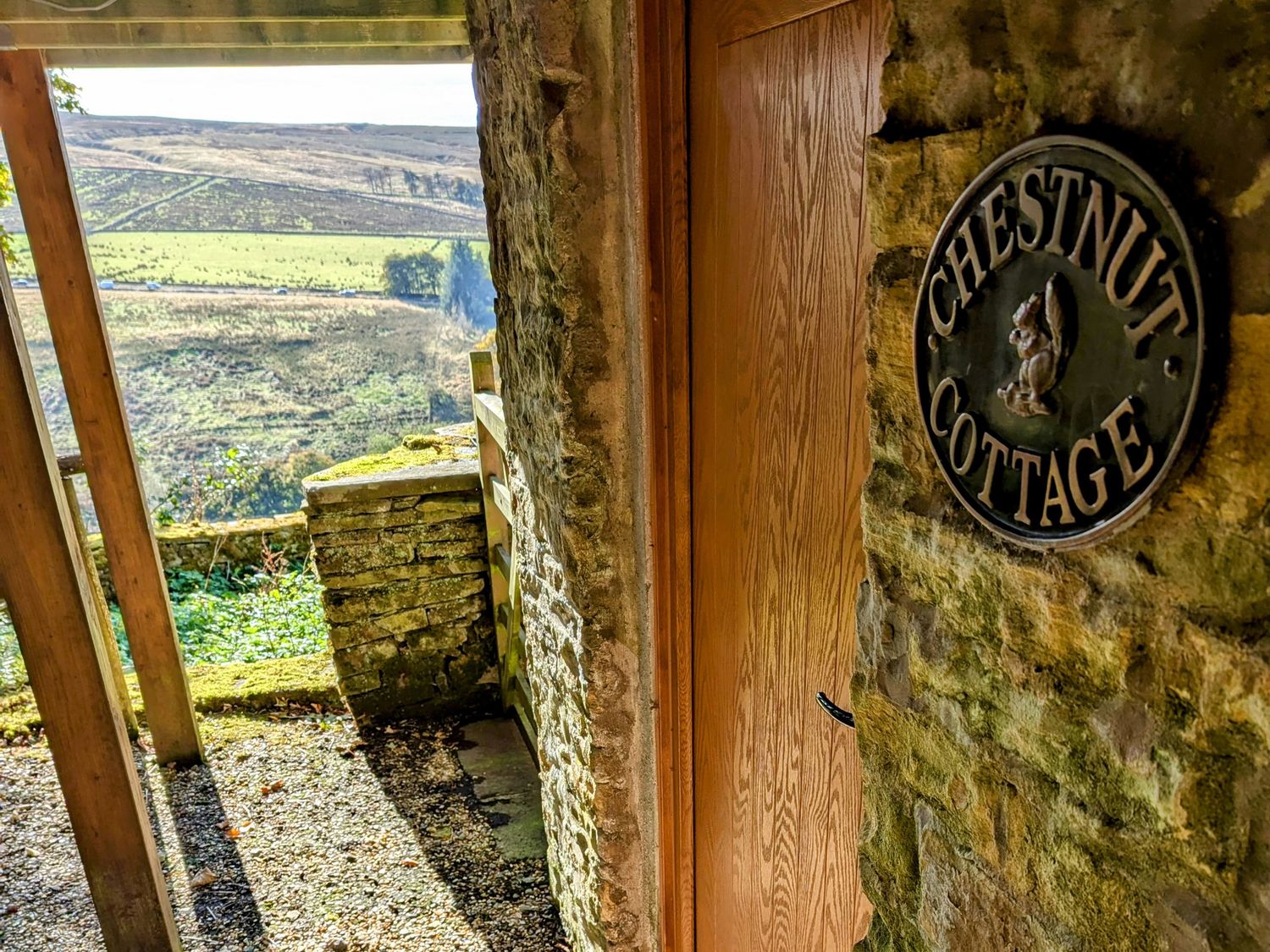 A wooden door with a sign that reads Chestnut Cottage on a stone wall with a countryside view in the background at Chestnut in Nenthall near Alston