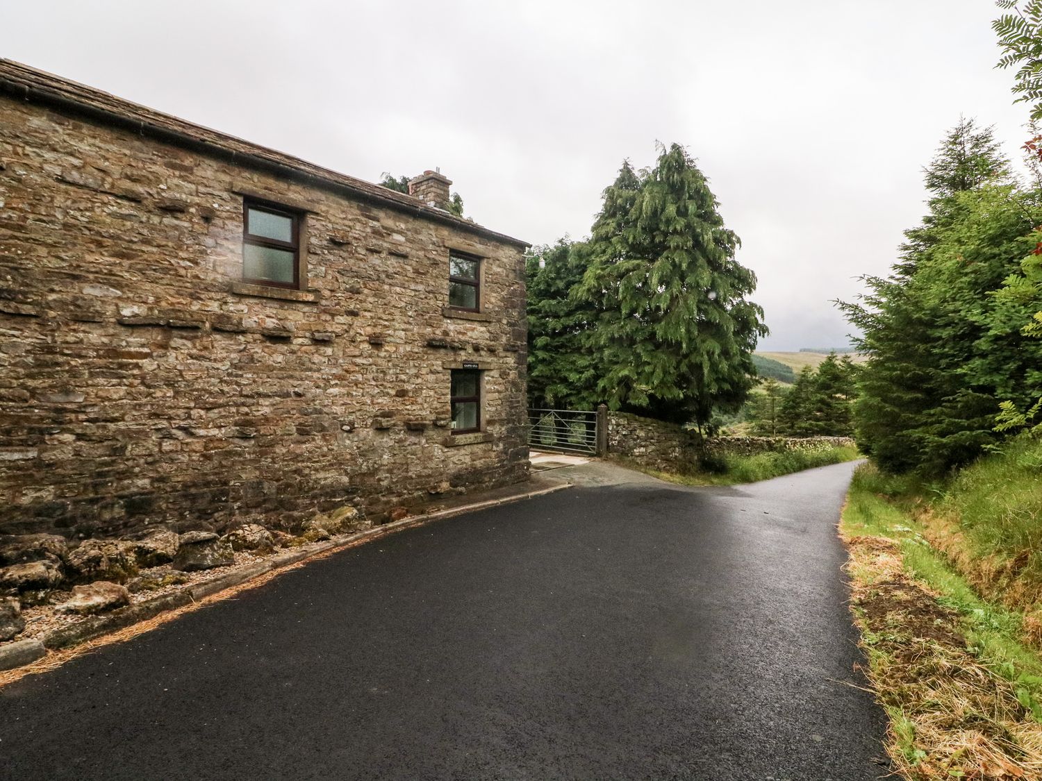 A stone building beside a paved road with trees and greenery at Garth Gill in Garsdale near Hawes