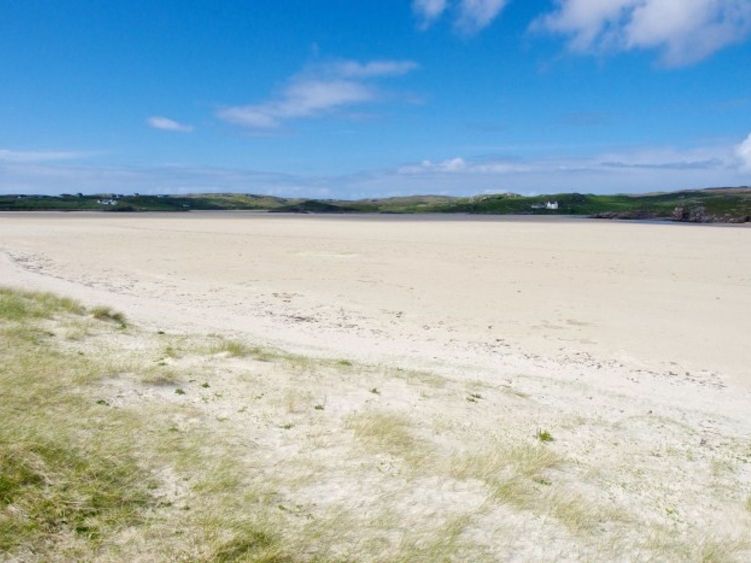 A sandy beach with grassy dunes and hills in the distance at 7A Ardroil Uig Isle Of Lewis