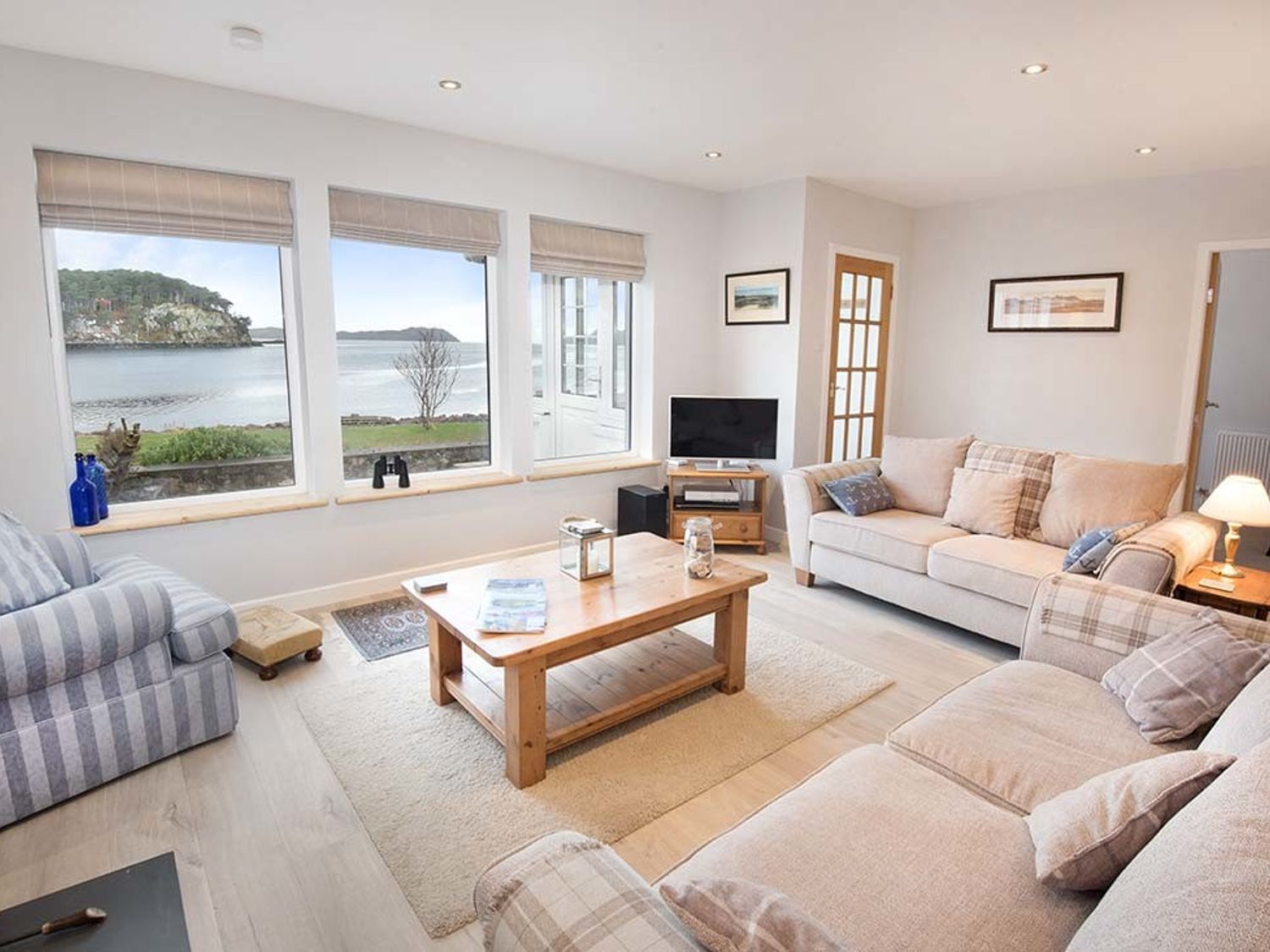 A living room with sofas a coffee table and windows overlooking water at Tigh en Leigh in Shieldaig