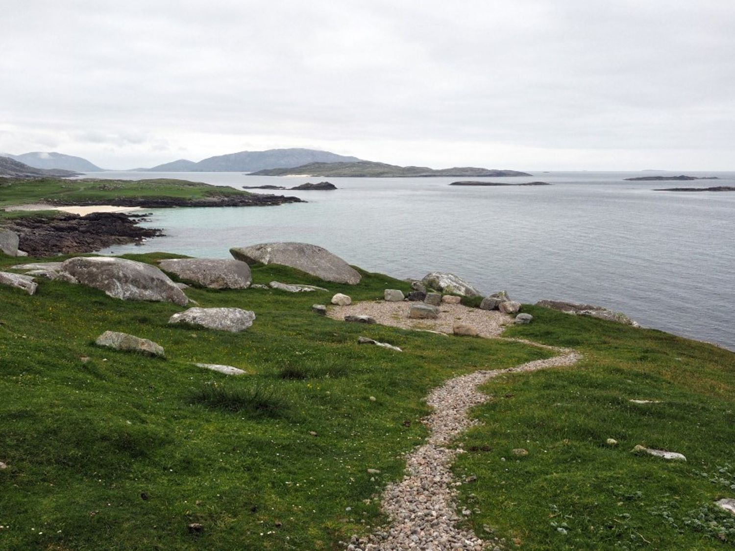 A coastal landscape with a rocky path leading to a fire pit by the sea at Spindrift Breanais nr Timsgearraidh