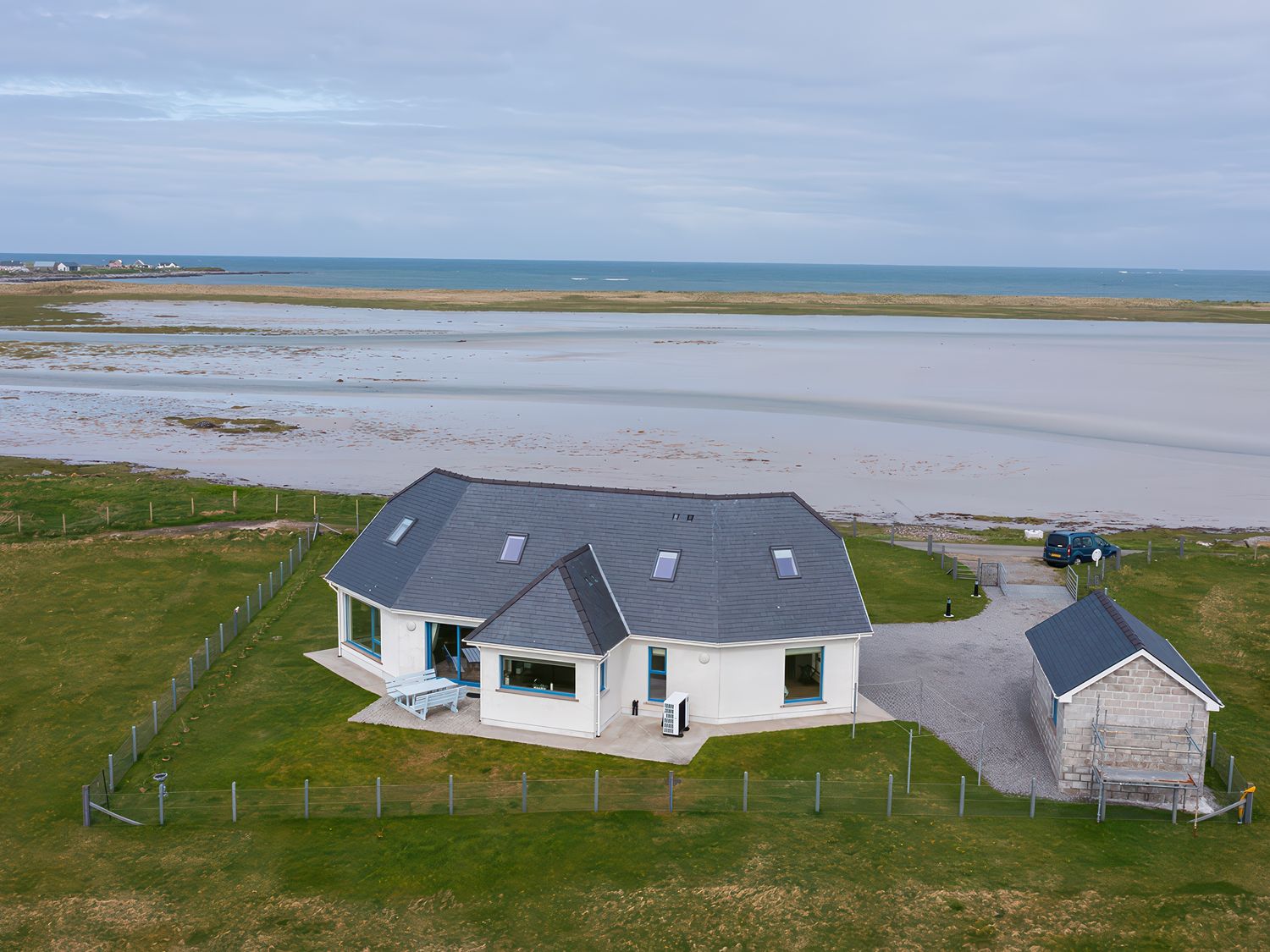 A house with a fenced yard near a beach and a small outbuilding at Gualan Sands in Iochdar