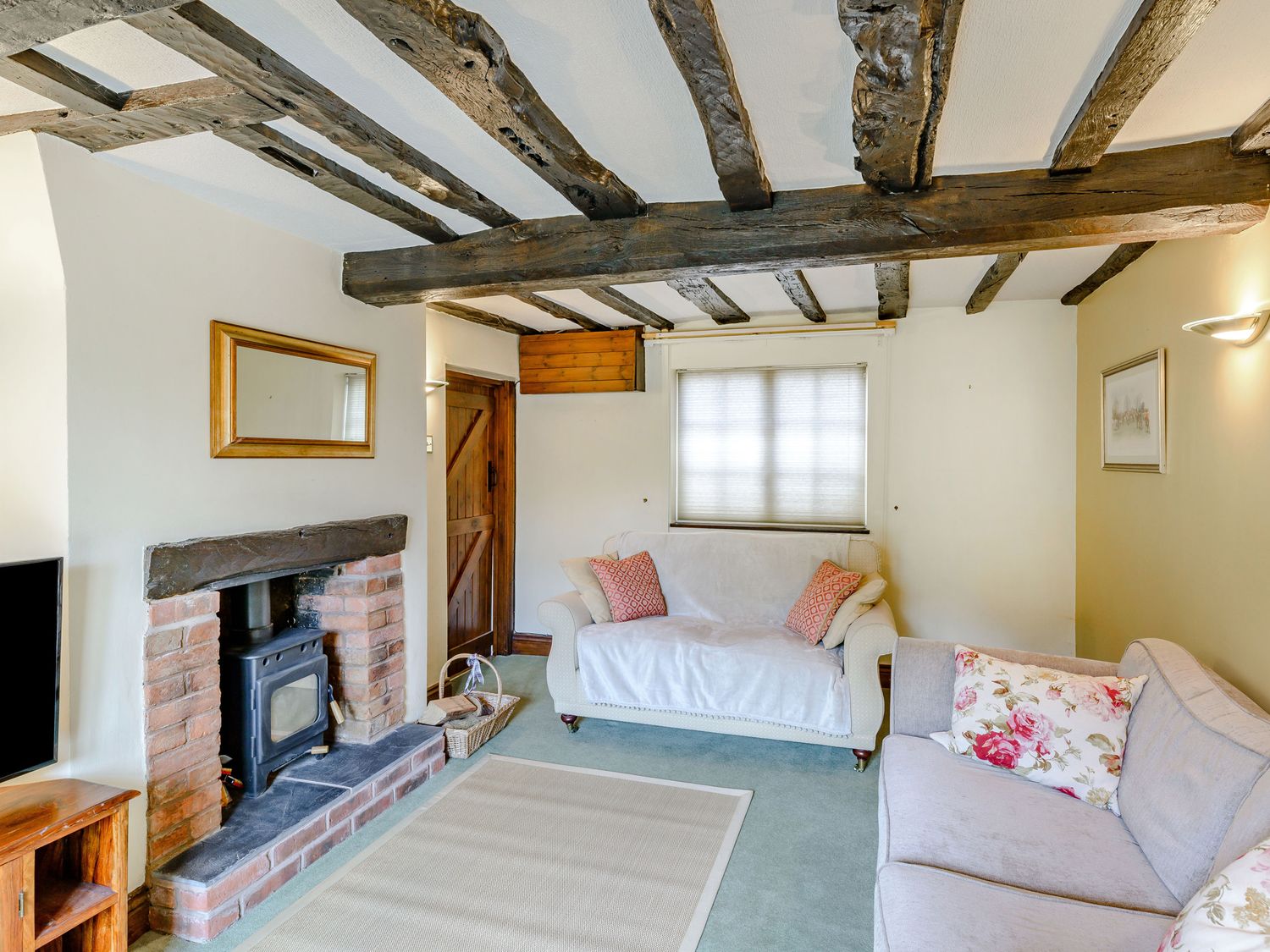 A living room with exposed wooden beams a brick fireplace two sofas and a window at Darwen in Abbots Bromley