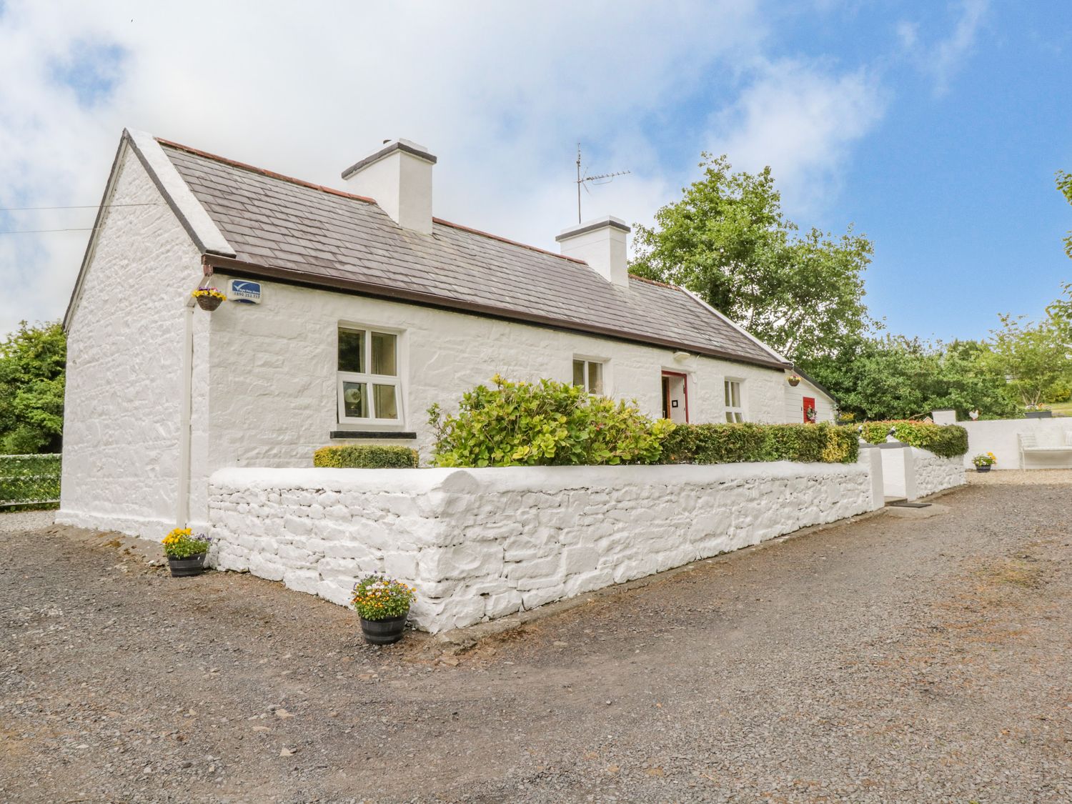 A white stone cottage with a slate roof surrounded by a white stone wall and bushes at Cartron Cottage in Ballintubber County Mayo