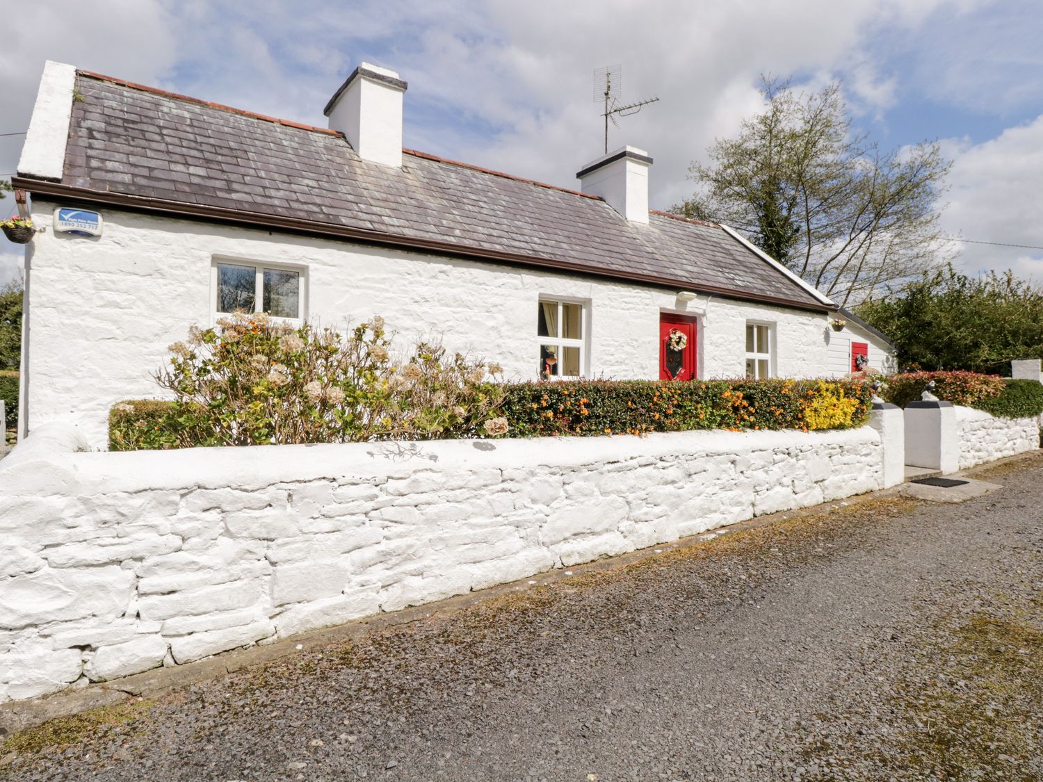 A white stone cottage with red doors surrounded by a white stone wall and bushes at Cartron Cottage in Ballintubber County Mayo
