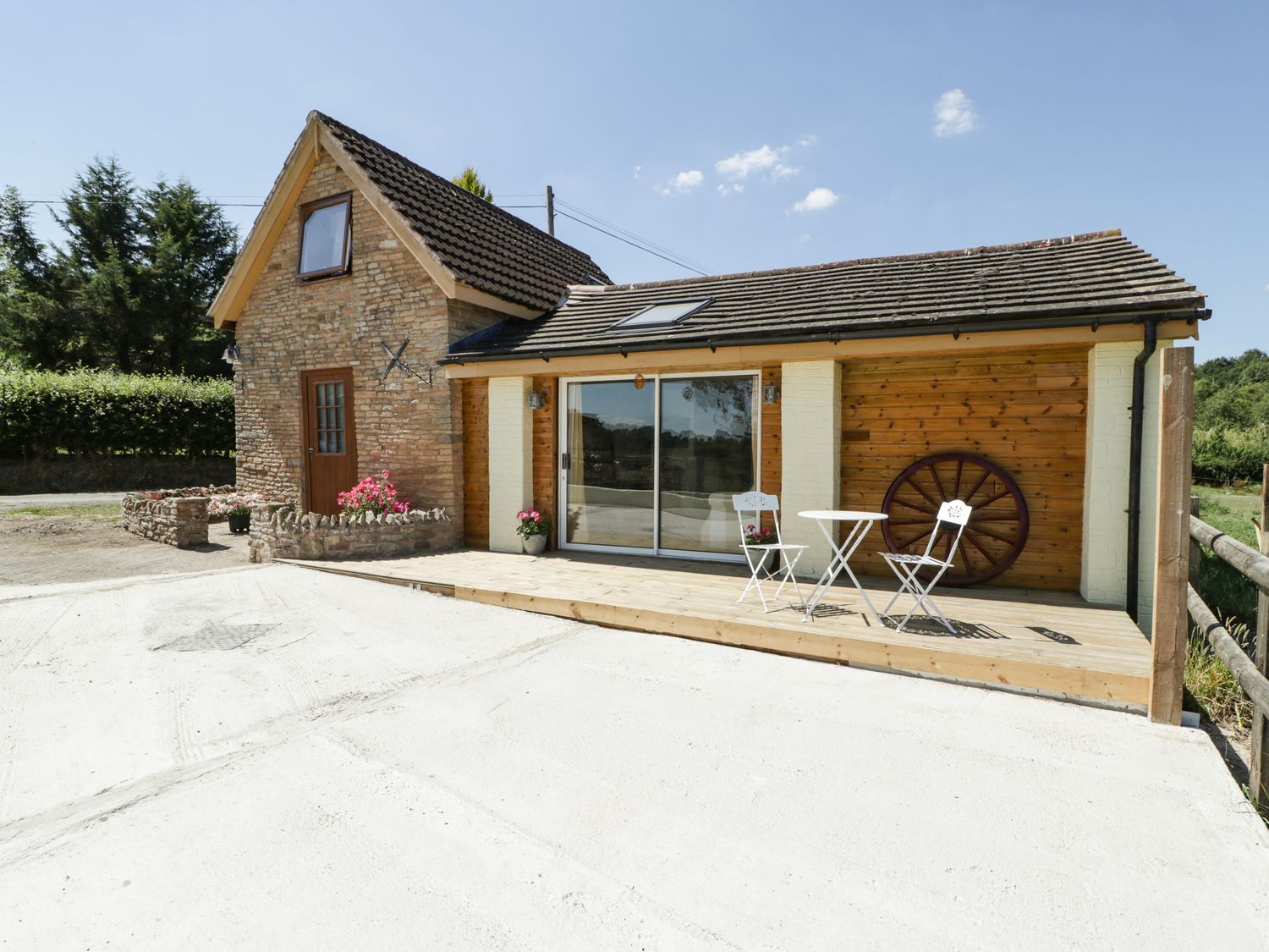A cottage with a wooden deck table and chairs and a large wagon wheel on the wall at Steel Works Farm in Gorsley