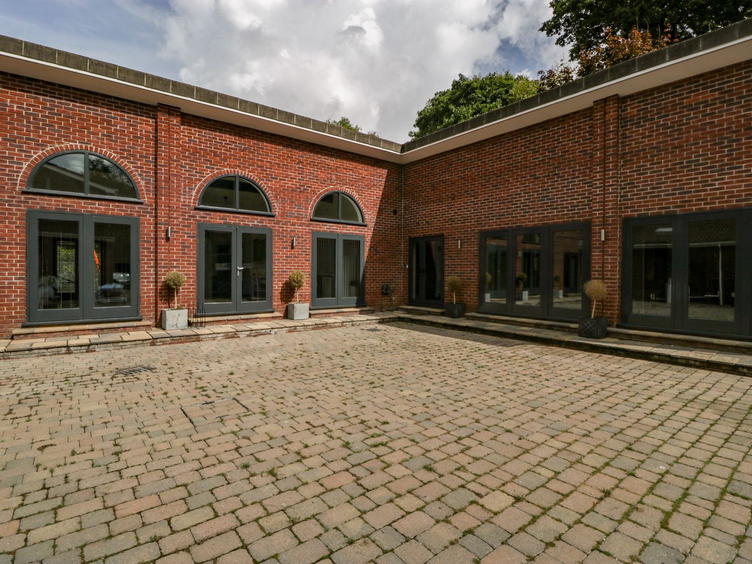 A paved courtyard with brick walls windows and doors and potted plants at The Cottage in Wimborne Minster