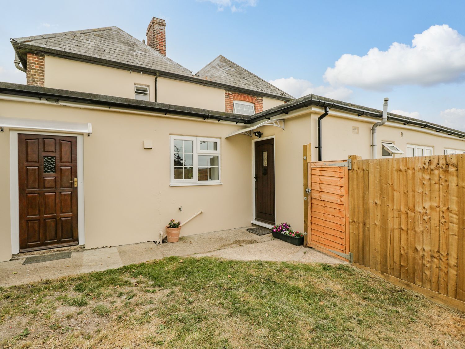 Exterior view of a beige house with two brown doors a window a small garden with grass and a wooden fence at Dorset View in Ibberton Hill near Ibberton