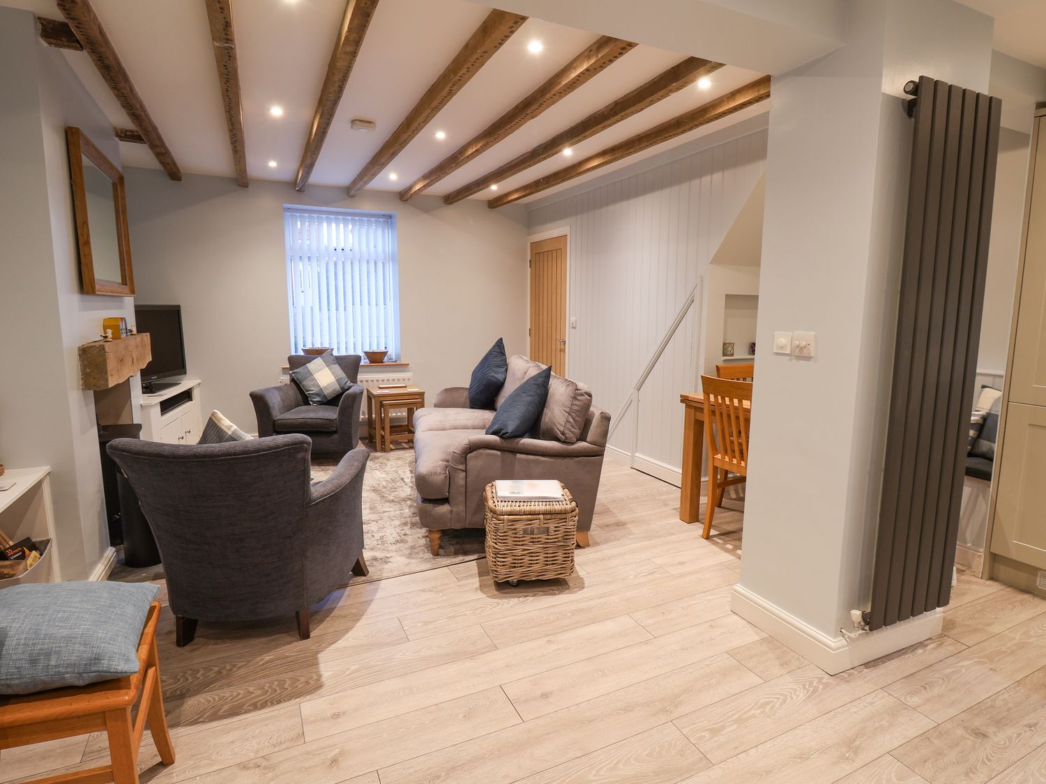 A living room with a sofa and armchairs a wooden dining table and chairs and exposed ceiling beams at Rockfish Cottage in Staithes