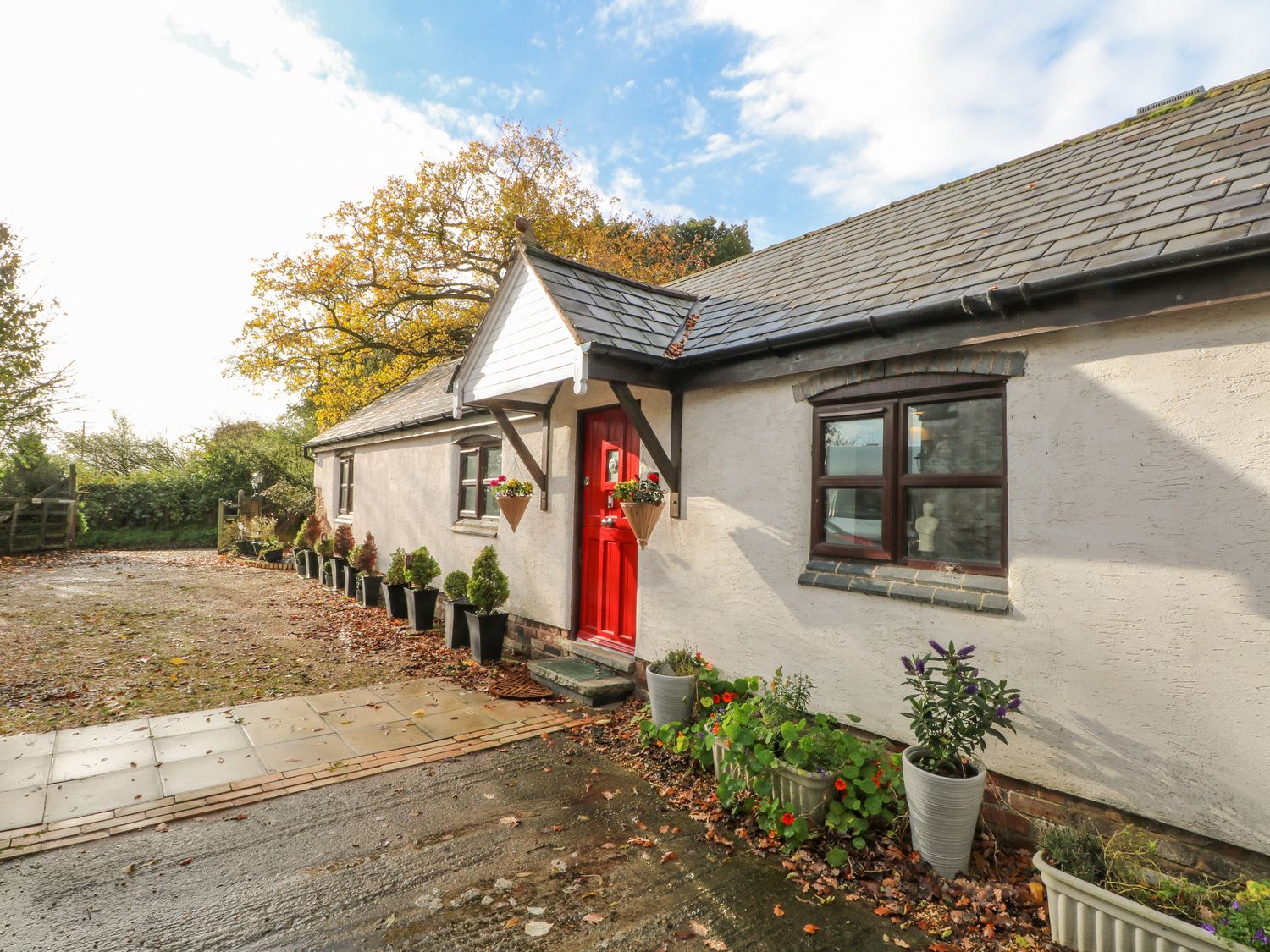 A single-story house with a red door and potted plants along the exterior at Burnt Oak Stables in Mynydd Isa