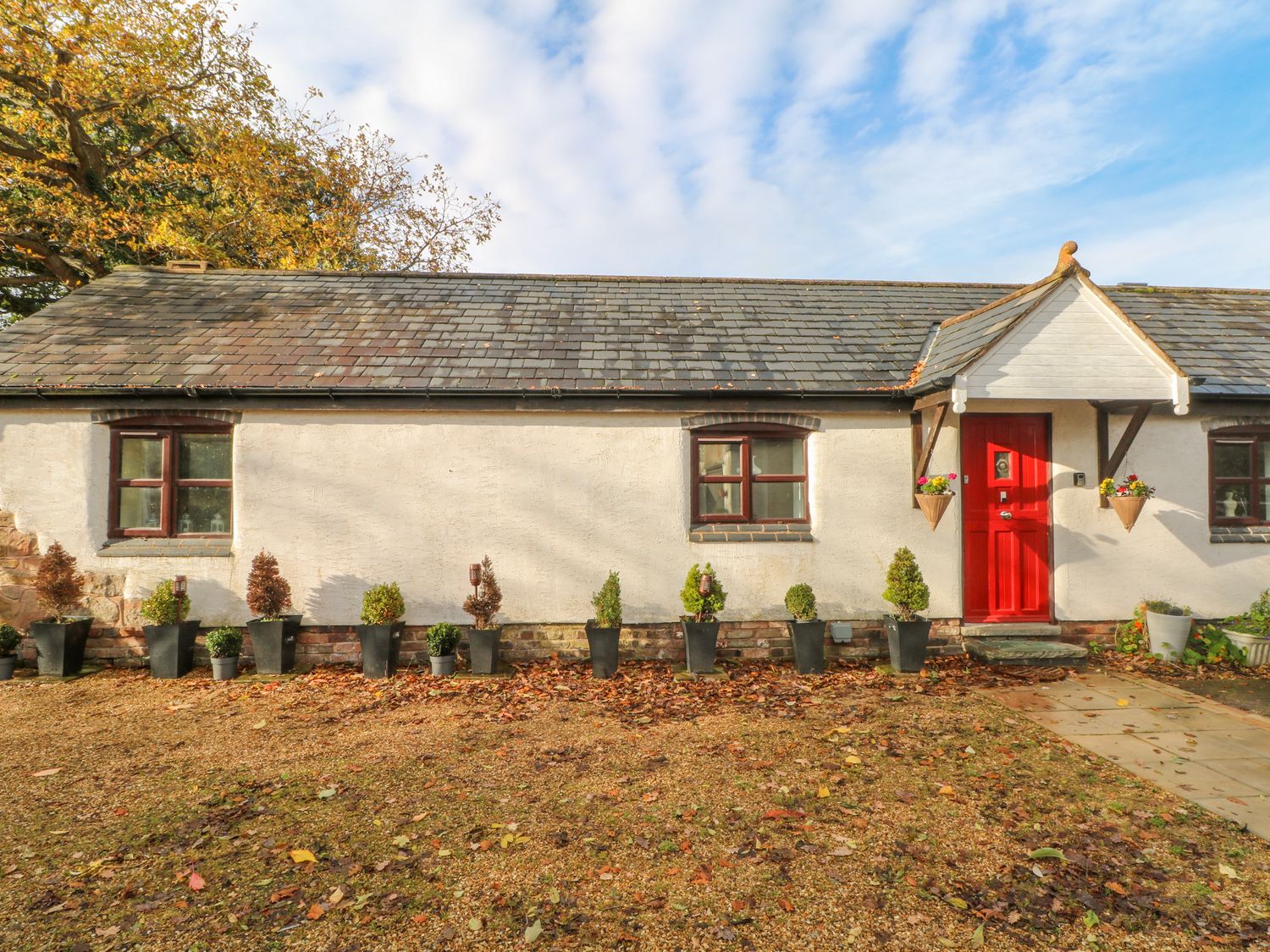 A single story building with a red door two windows and potted plants outside at Burnt Oak Stables in Mynydd Isa